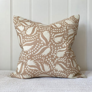 This shows a 45 x 45cm square cushion featuring a striking design with a blush pink background adorned with an intricate pattern of cream, leaf-like shapes and clusters of small dots. The pattern is dynamic and organic, giving it an elegant appearance. The fabric is a cotton linen blend, providing a textured feel.