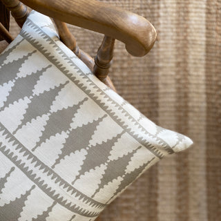 A close-up from above of the corner of a cushion with a bold diamond pattern in natural and cream on a wooden armchair. Out of focus on the floor is a striped jute rug.