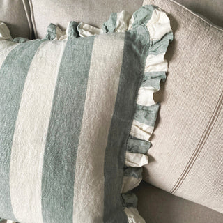 A close up of two cushions on a light grey sofa. The front cushion has wide green and white stripes with a frill and the cushion behind us cream with a stripe down the middle.