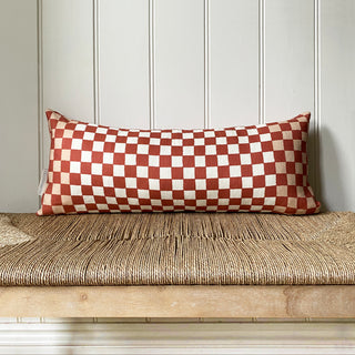 Red and cream checkered pillow on a wooden bench against a panelled wall.