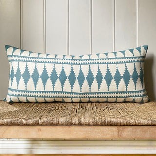 Decorative pillow with blue and white pattern on a wooden bench against a paneled wall.