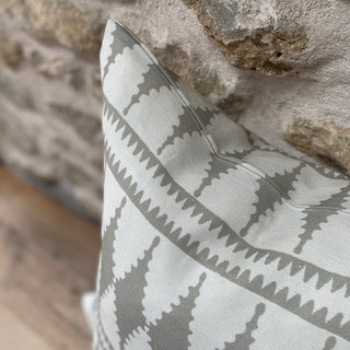 A close-up of the corner of a cushion leant against an exposed stone wall. The pattern has a bold diamond pattern in natural and cream colours.