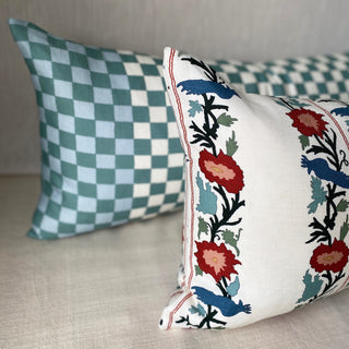 Two decorative pillows, one checkered and one with floral embroidery, on a neutral background.