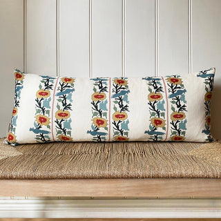 Decorative pillow with floral pattern on a wooden bench against a white paneled wall.