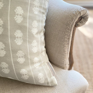 A close up of the corner of a cushion sitting on a natural linen armchair with exposed stitching on the arms. The cushion is a natural colour with a oval stripe in cream. A branded Clothsmith label can be seen in the bottom right corner.