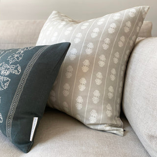 Two cushions leant into the corner of a natural linen sofa. The back cushion is bigger, with an oval stripe in cream on a natural background. The front rectangular cushion is in slate green with a cream pattern.