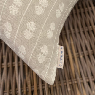 A close up of the corner of a cushion sitting ona wicker basket. The cushion is natural with a cream stripe, and features a branded Clothsmith label in the bottom corner.