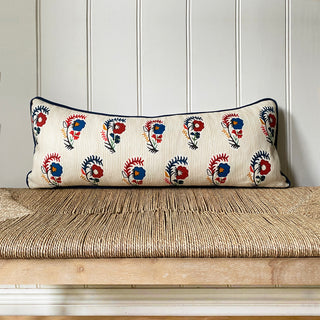 Decorative pillow with floral pattern on a woven bench against a paneled wall.