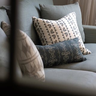 A shot through a window of a duck egg sofa with cushions on it. The most prominent cushion is cream with a detailed dark blue patterned stripe. The window frame in the foreground is out of focus.