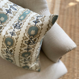 A close up from above of a square cushion with floral pattern in blue and natural tones and a heritage style design sits on a natural linen armchair.