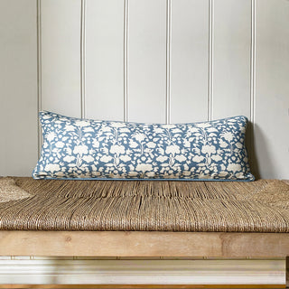 Long blue and white floral pillow on a wooden bench against a paneled wall.