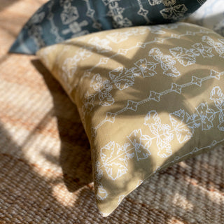 A square cushion with a floral stripe in hay yellow lying on a natural jute rug in the sunshine.