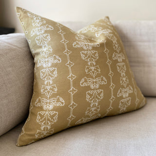 A square cushion with a floral stripe in hay yellow sits on a natural linen sofa.
