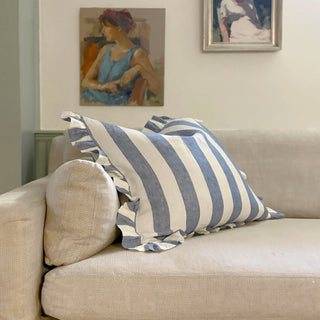 A large blue and white striped cushion with frill leaning on a natural linen sofa
