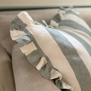 A large square cushion with green and white stripes and a frilled edge, displayed on a sofa.