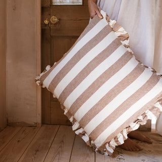 Striped pillow with frills held by a person in a home setting standing on a wooden floor