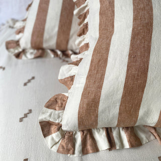 Close-up of terracotta and white striped pillows with frilled edges on a light background